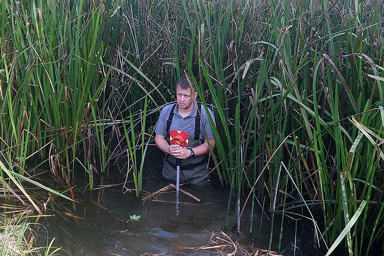 Földmérés vízben állva, prizmát tartva